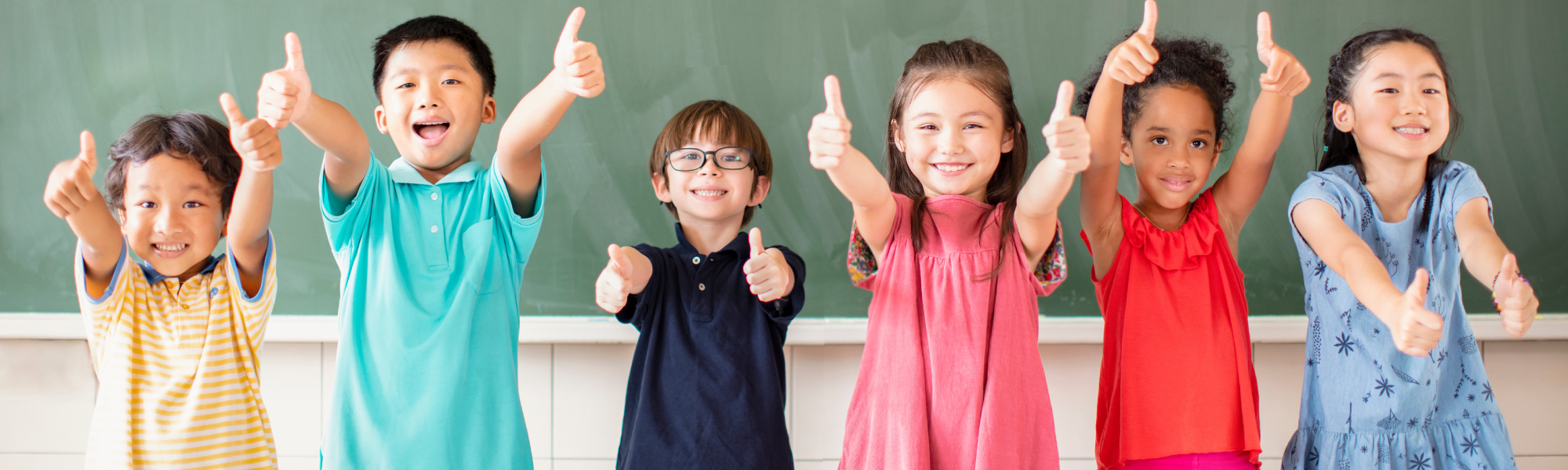 Elementary age students in front of an old-fashioned green chalk board smiling with their thumbs up.