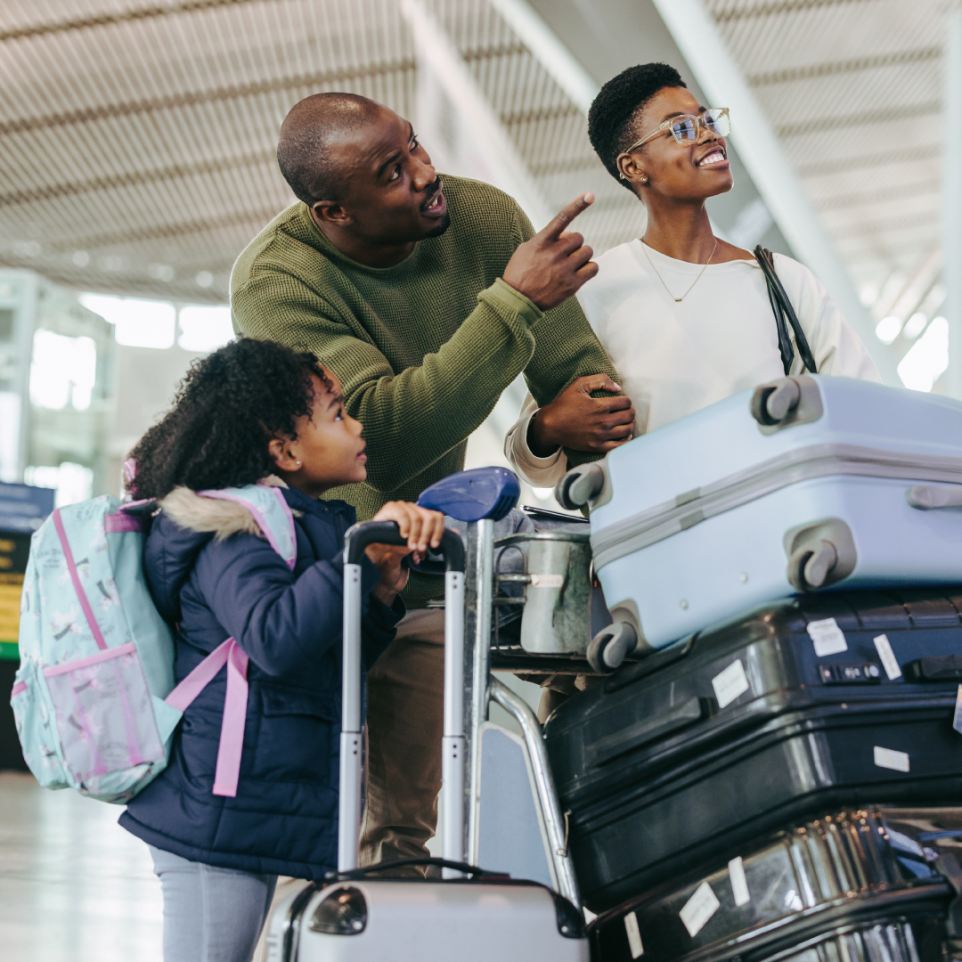 Nuclear family of a black man, woman, and little girl preparing to travel in an airport, with a cart full of suitcases.